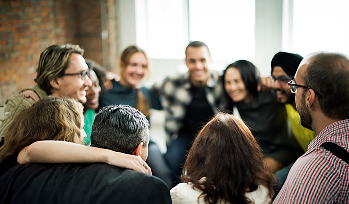 Un groupe de personnes assises en cercle, souriantes et enlacées dans une atmosphère conviviale.